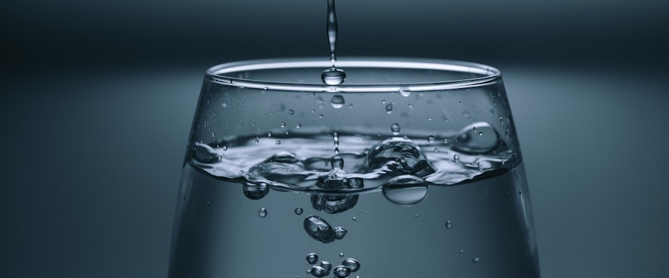 Clear filtered water being poured into a glass from a glass pitcher in a bright kitchen