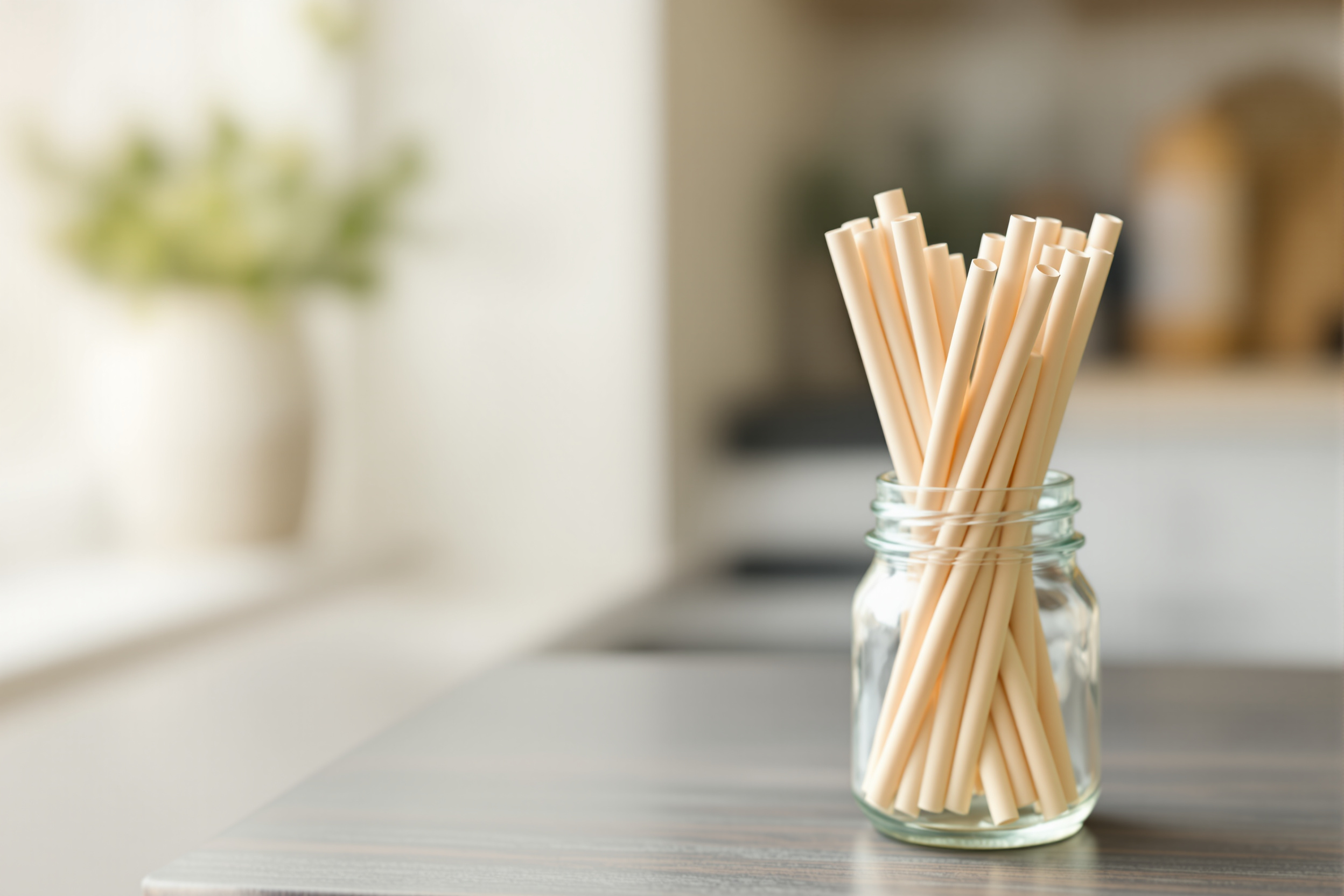 A handful of plain paper drinking straws standing upright in a clear glass jar on a kitchen counter