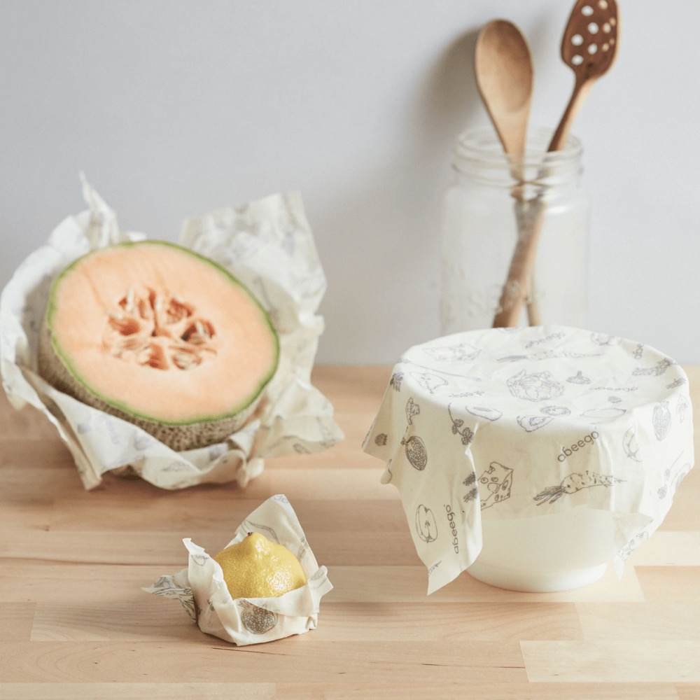 Abeego beeswax food wrap variety pack in use — a wrap molded around a halved cantaloupe and a wrap covering a bowl