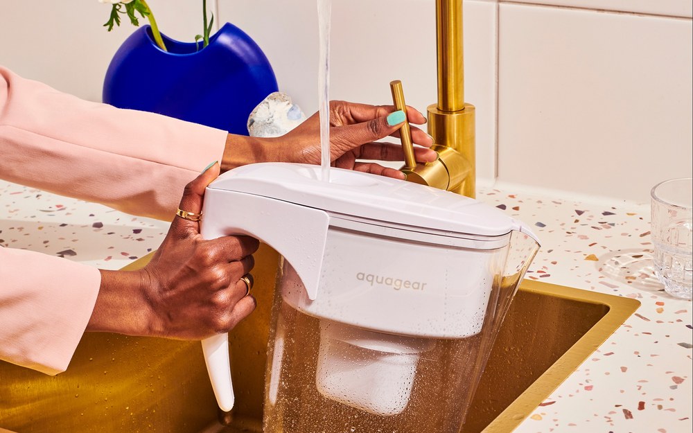Aquagear water filter pitcher being filled at the sink — 150-gallon filter, USA-made media, lifetime pitcher guarantee
