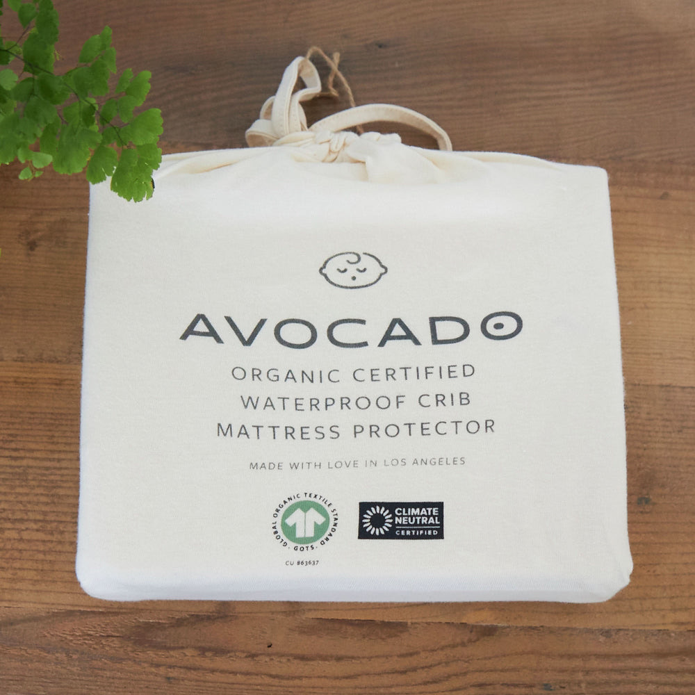 Avocado Organic Certified Waterproof Crib Mattress Protector in its GOTS-certified organic cotton drawstring packaging