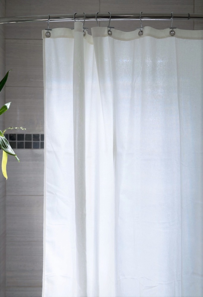 Bean Products organic cotton shower curtain liner in white, hanging on a chrome rod in a tiled bathroom