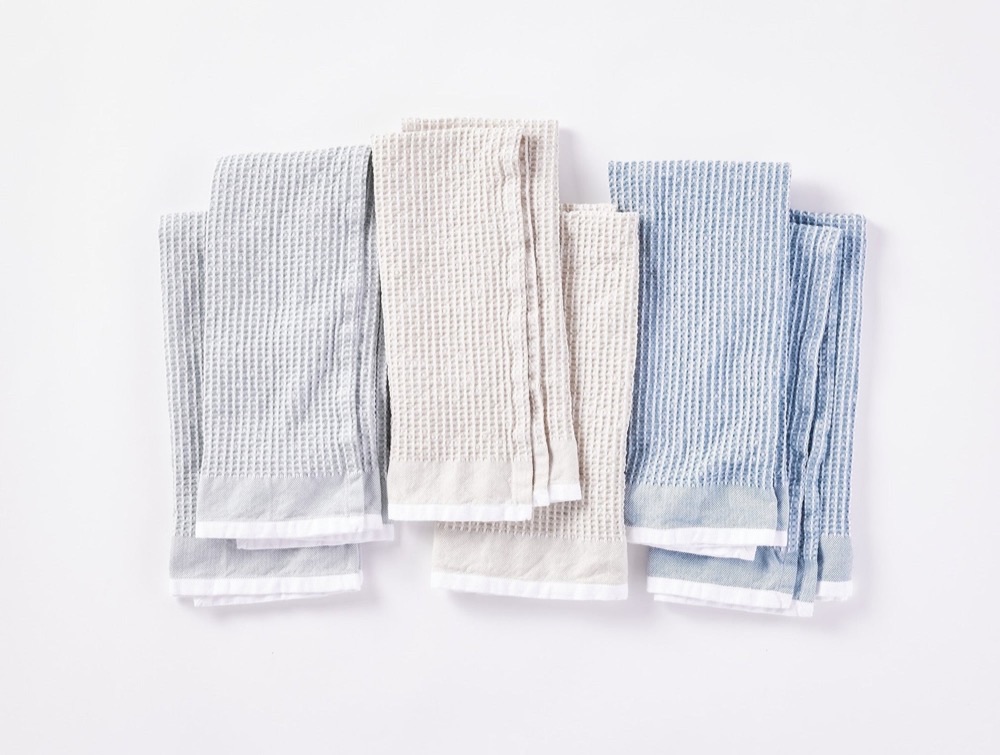 Coyuchi organic cotton waffle-weave kitchen towels folded on a white surface in soft natural tones