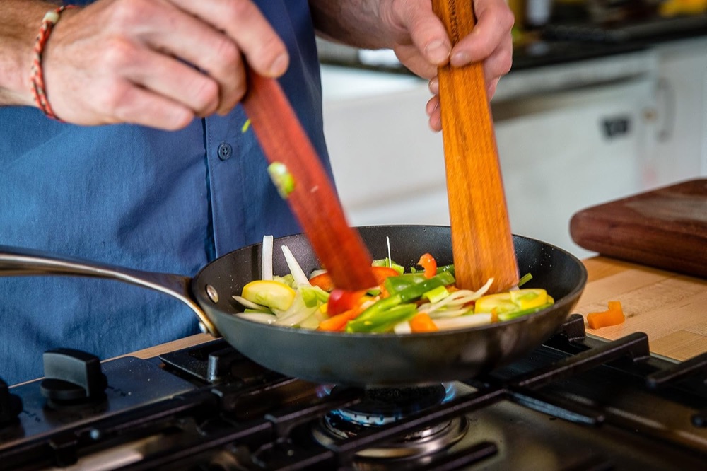Two Earlywood flat wooden spatulas stirring vegetables in a skillet