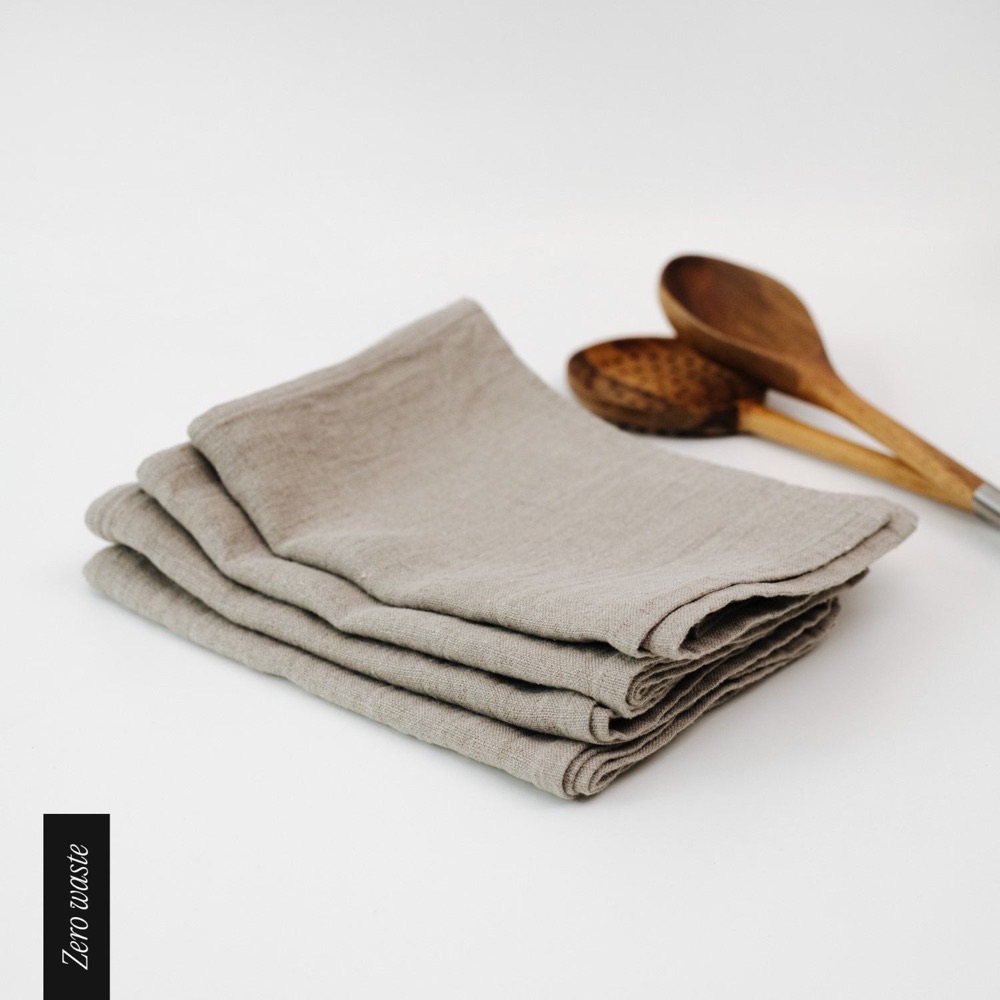 Linen Tales natural European linen kitchen towels folded in a stack beside two wooden spoons on a white surface
