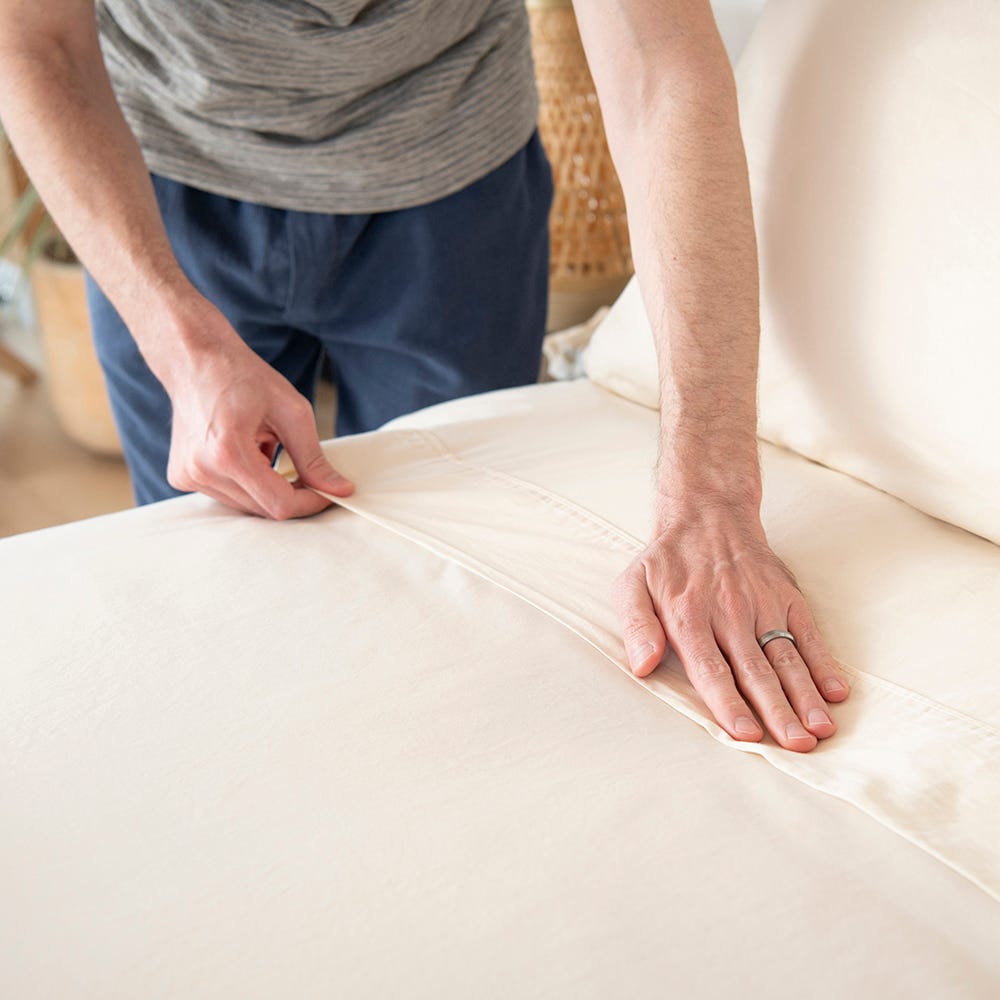 Naturepedic Organic Cotton Sheet Set — GOTS-certified ivory sateen being fitted onto a bed, tested free of 100+ harmful chemicals
