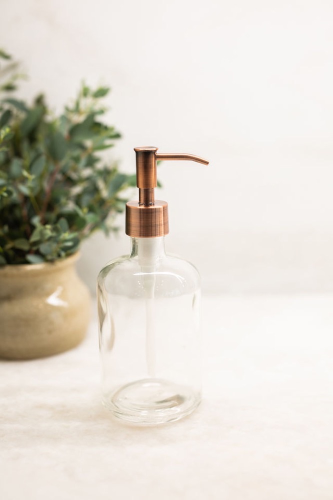 Rail19 clear recycled glass soap dispenser with a metal pump styled on a bathroom counter beside a eucalyptus plant
