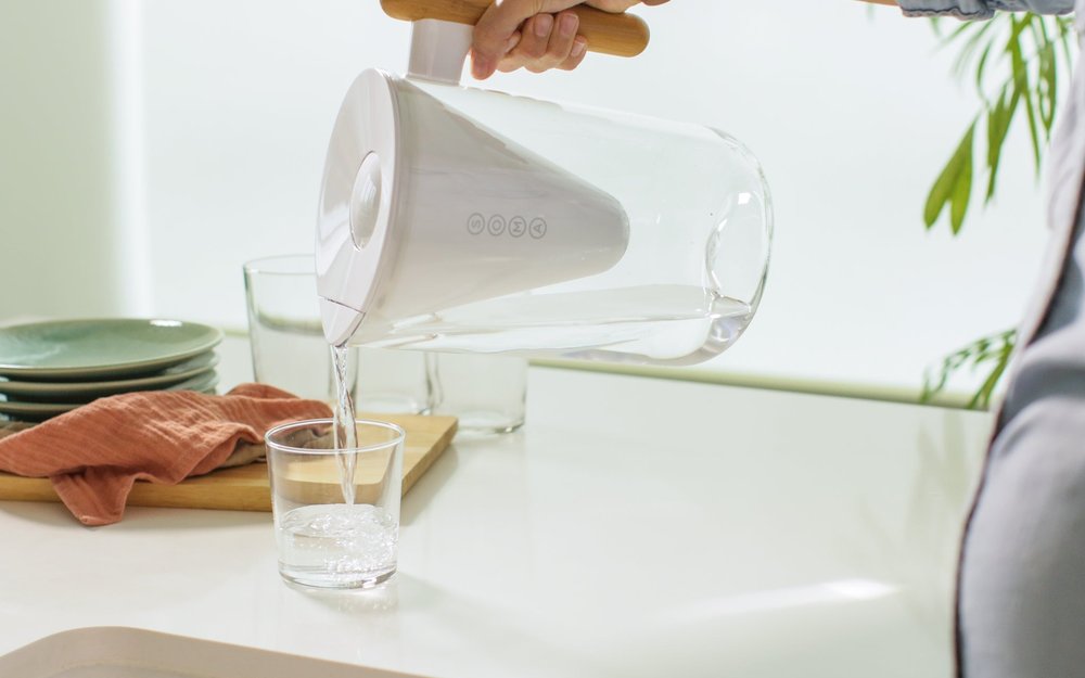Soma water filter pitcher with sustainable wood handle pouring filtered water into a glass — plant-based coconut carbon filter