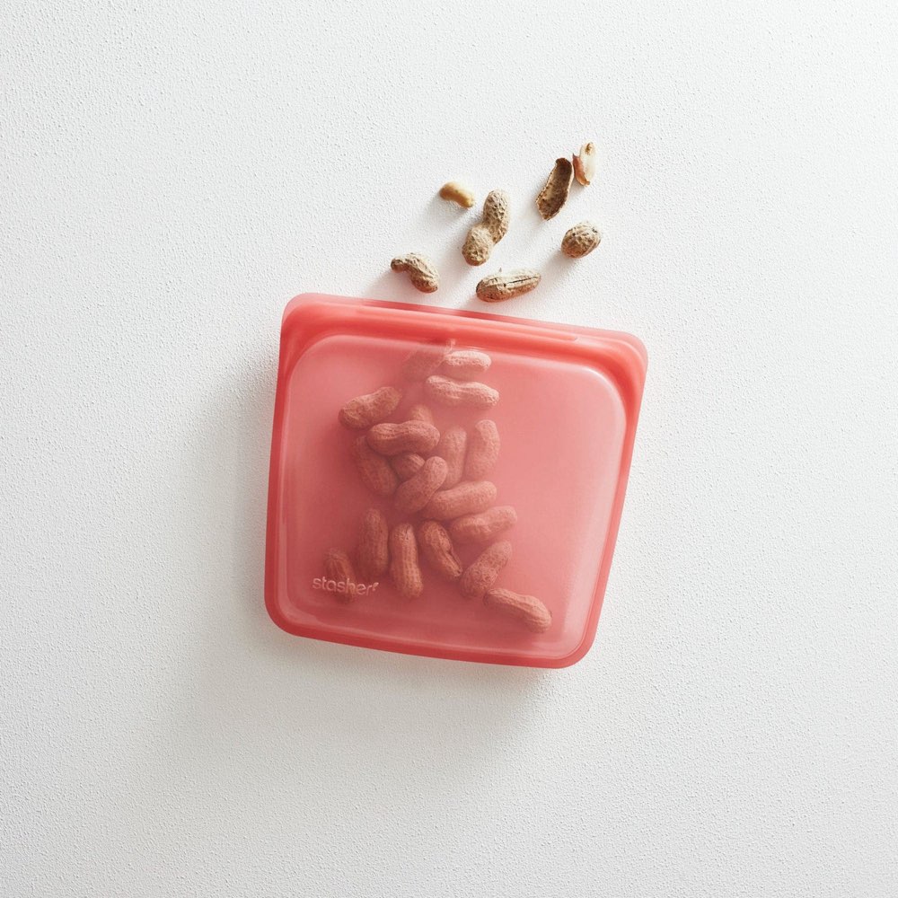 Stasher Sandwich Bag in coral platinum silicone holding peanuts — airtight pinch-seal, 100% food-grade silicone, no plastic