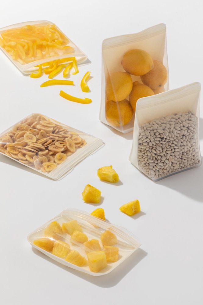W&P Porter silicone bags in cream holding produce — one-piece LFGB-certified silicone, dishwasher and freezer safe, no plastic
