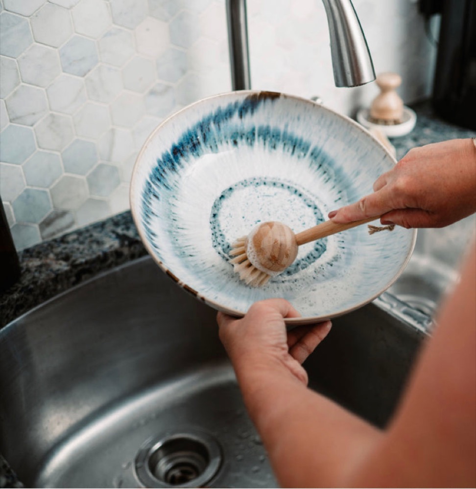 Zefiro bamboo dish brush with sisal bristles cleaning a ceramic bowl at the sink — plastic-free, replaceable head